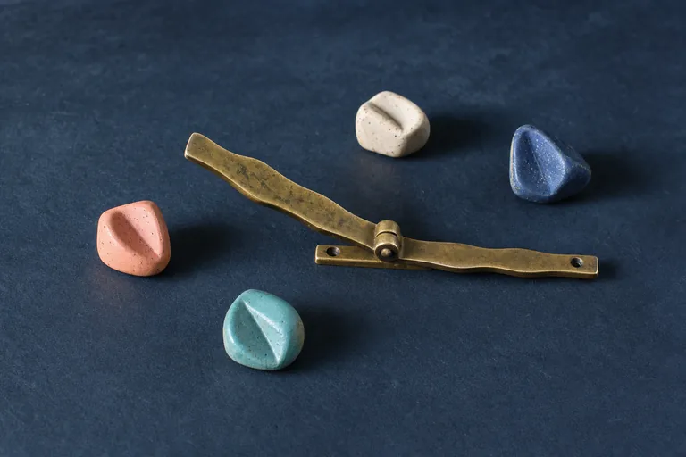 Abstract ceramic lozenges rest without clustering beside a linear brass gate shown open and calmly settled.