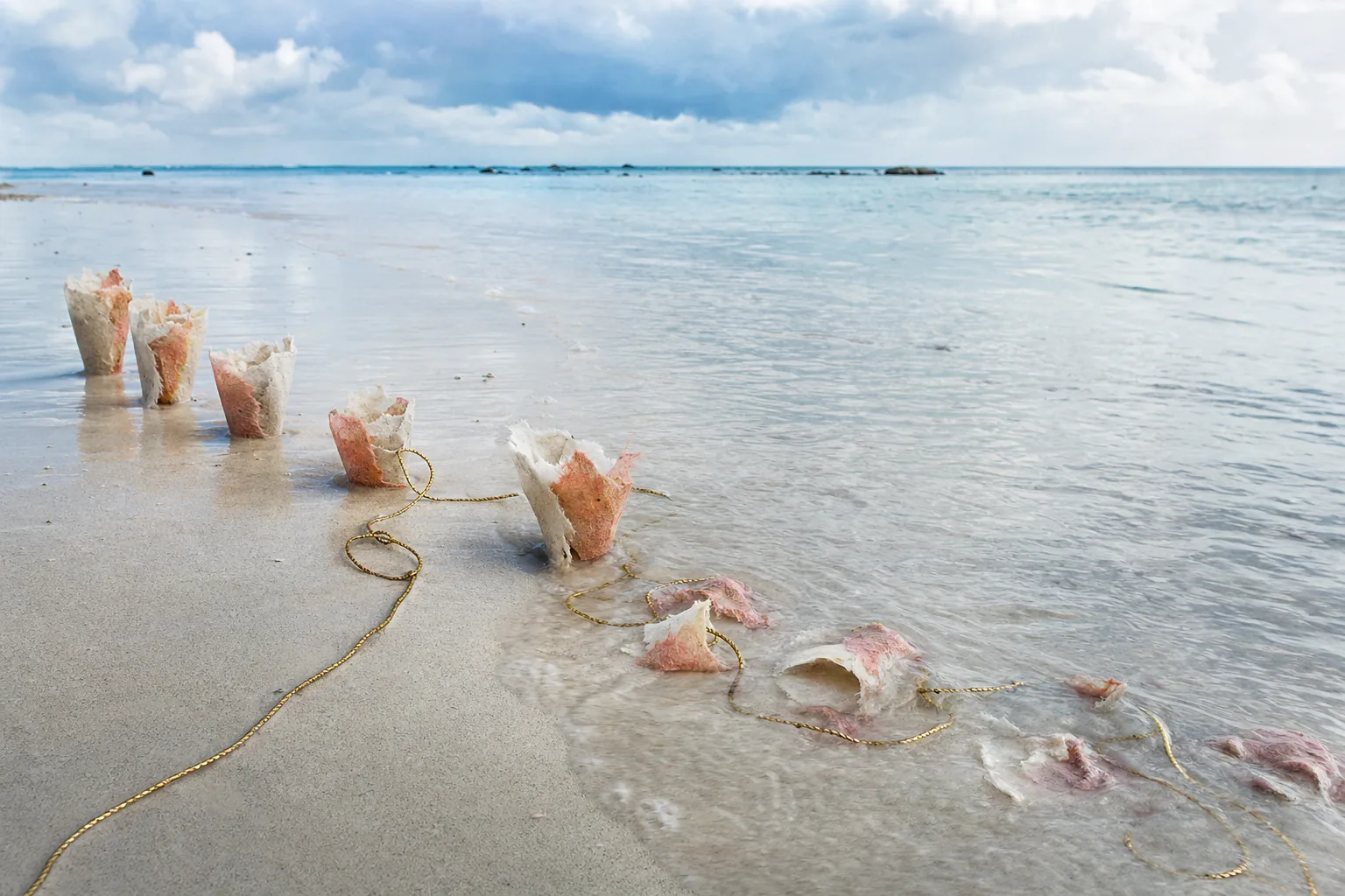 Tidal water gradually softens temporary sand-and-paper forms while a gold cord disappears and reemerges.