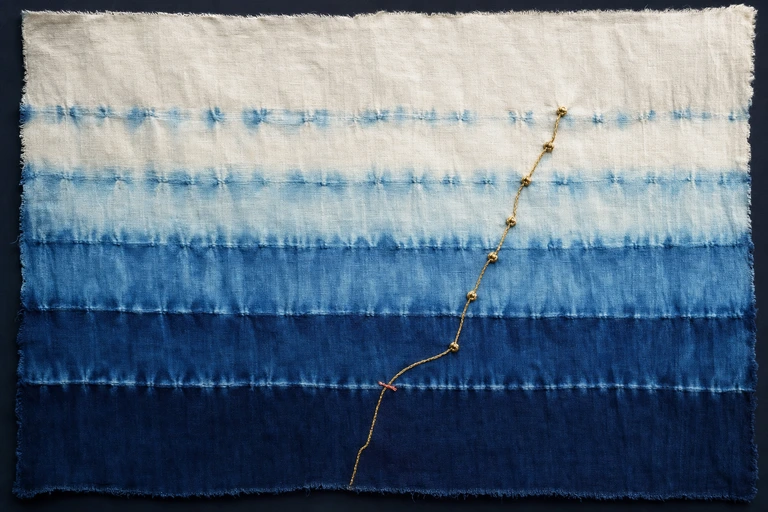 A gold thread with small knots rises through indigo bands from deep midnight to pale white, turning up before the darkest band.