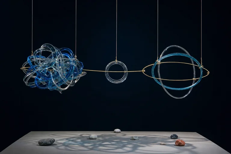 Tangled glass rings, a withdrawn ring, and an open orbit form one suspended kinetic sculpture.