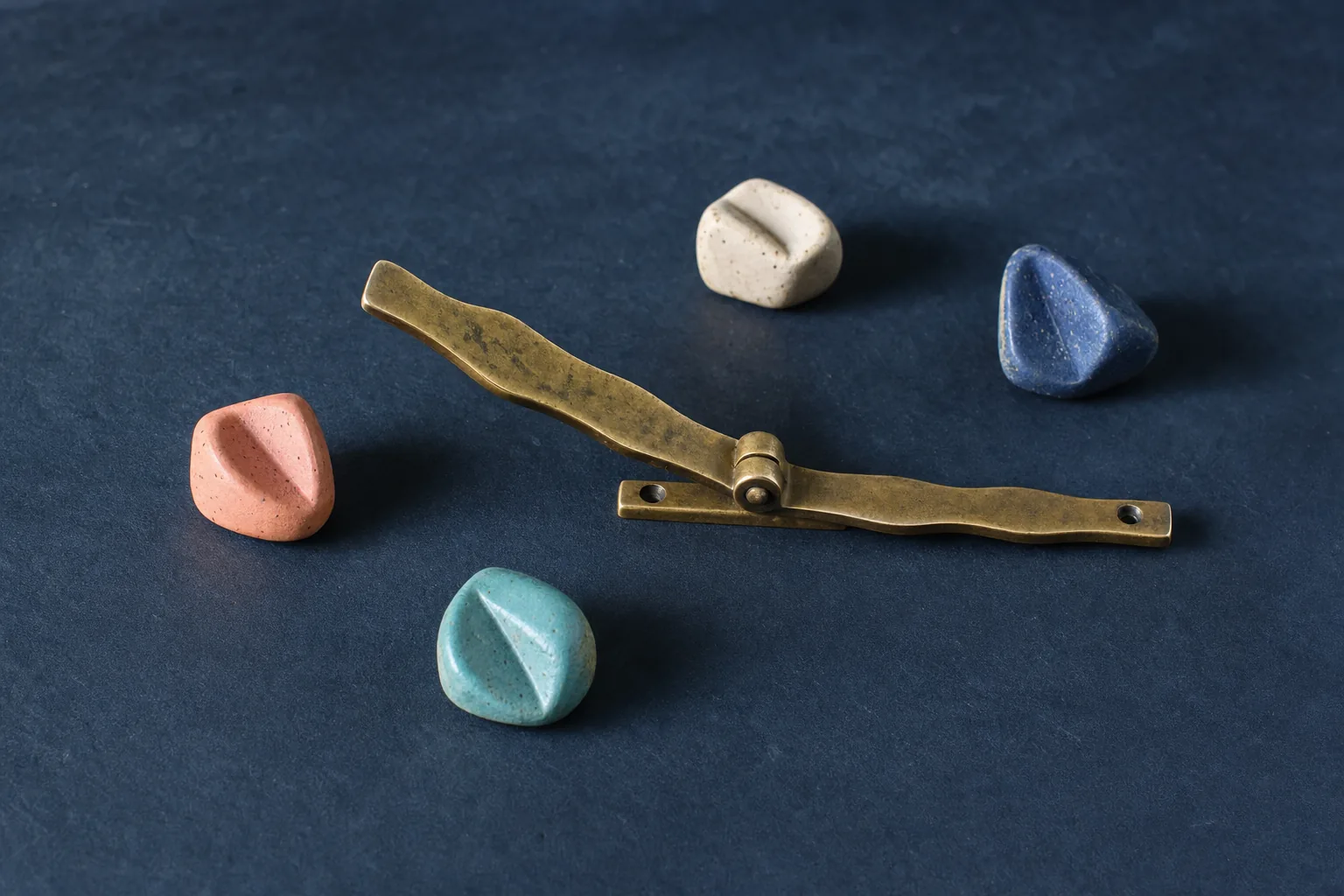 Abstract ceramic lozenges rest without clustering beside a linear brass gate shown open and calmly settled.