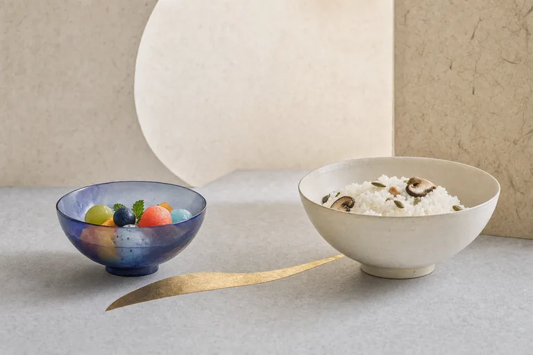 A translucent fruit bowl and plain rice bowl share a sparse alcove, joined by gold inlay.