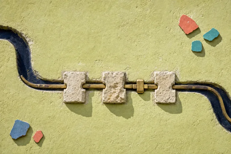 A worn brass groove rejoins its original wall channel through three rough limestone inserts and one plain latch.