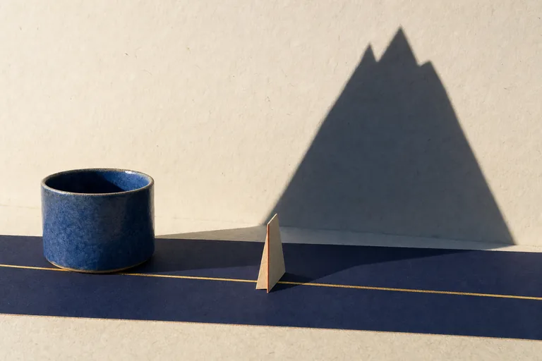 A level gold path crosses ordinary paper ground while a small form casts an enormous mountain shadow.