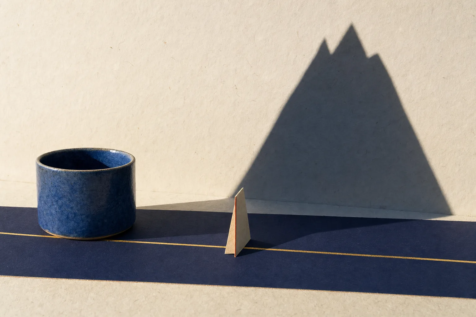 A level gold path crosses ordinary paper ground while a small form casts an enormous mountain shadow.